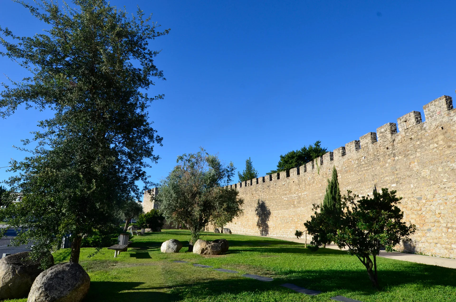 Muralha antiga de Évora com ameias, gramado e árvores sob céu azul, em Portugal