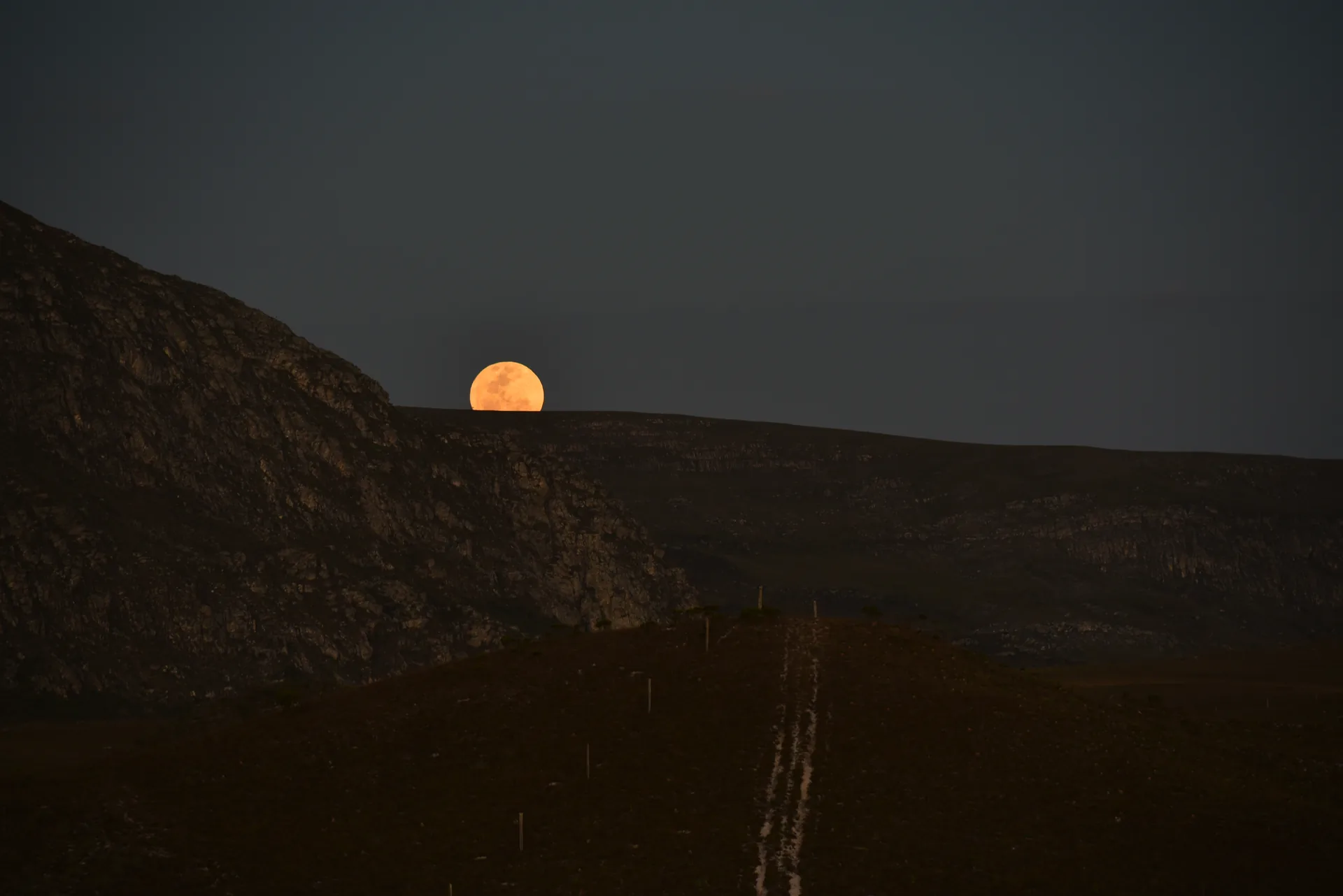Lua cheia alaranjada surgindo atrás da encosta escura, no céu do anoitecer, no Vale do Travessão