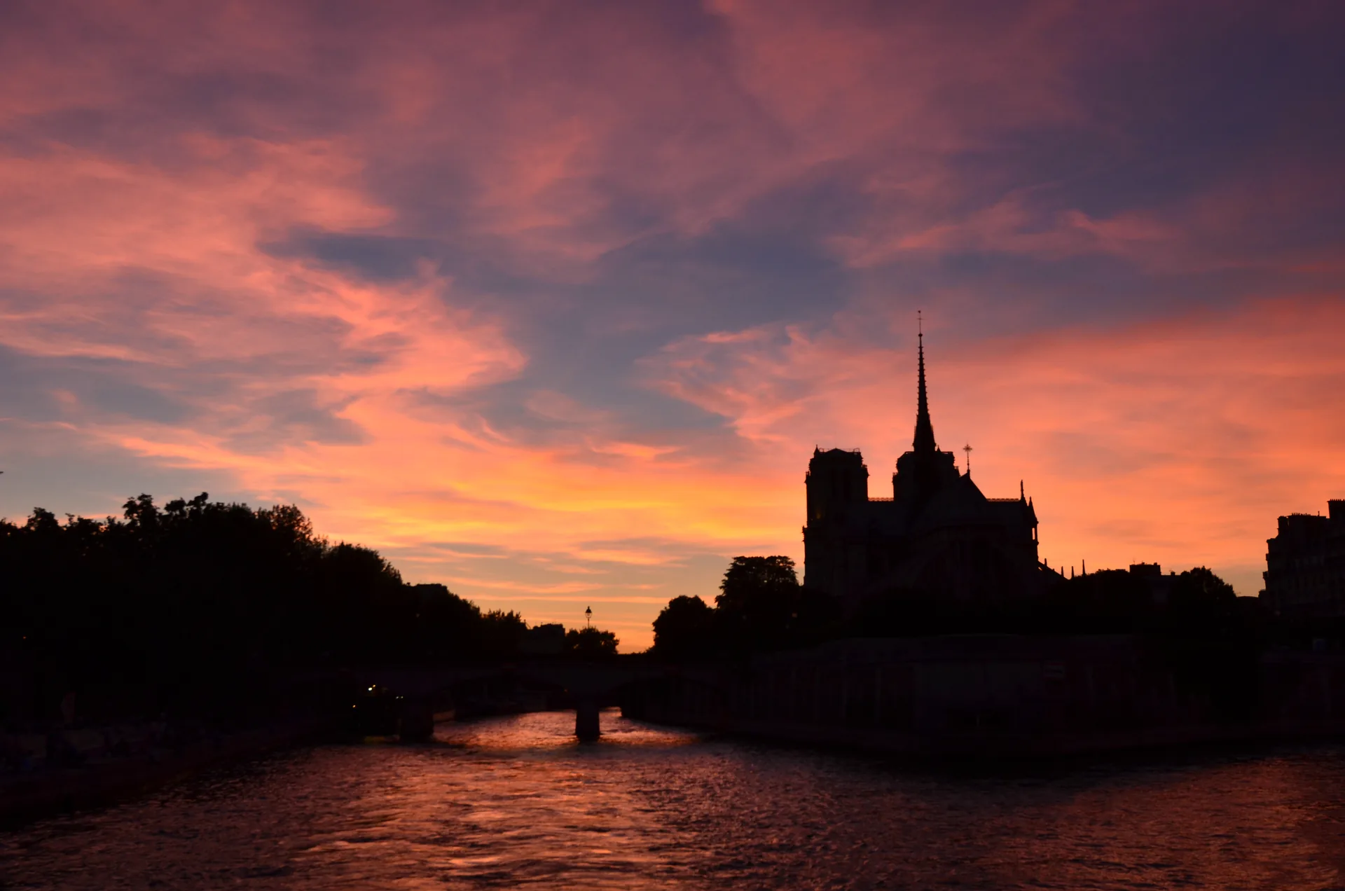 Silhueta da Catedral de Notre-Dame ao entardecer, com o céu rosado refletido no rio Sena, em Paris