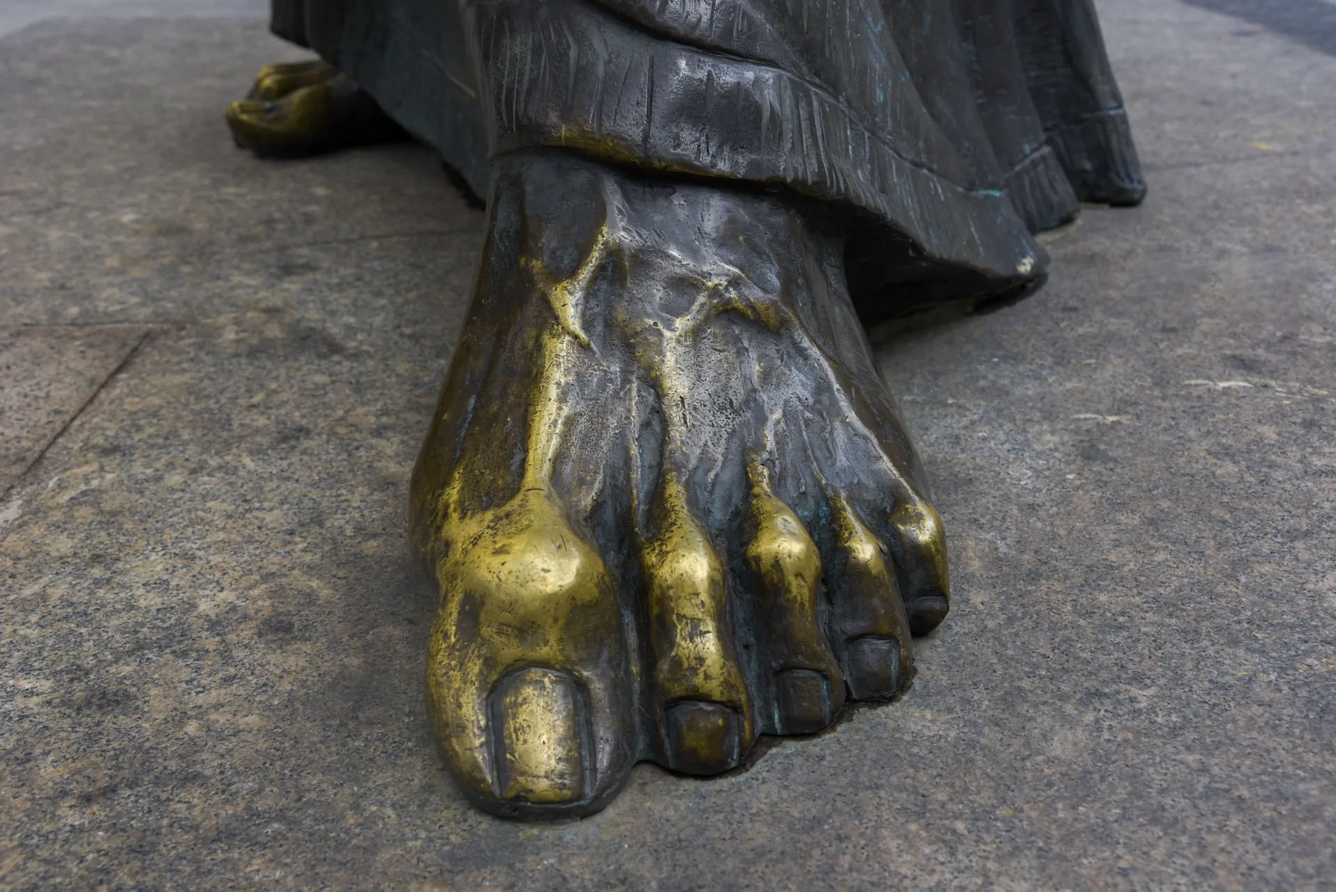Pé de bronze da estátua do Apóstolo Paulo, com os dedos dourados e brilhantes, sobre o pedestal de pedra