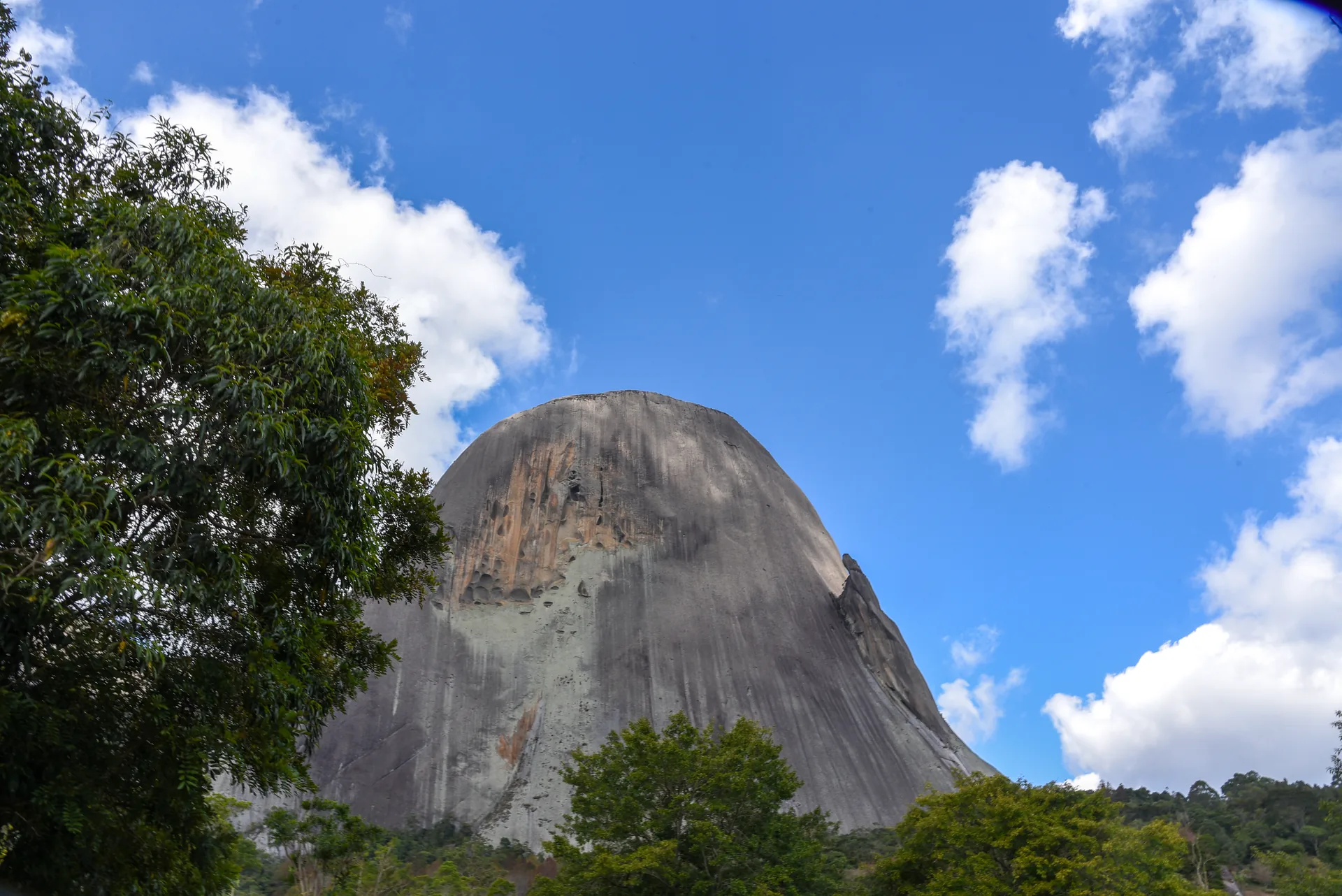 Pedra Azul, grande monólito de granito, entre árvores e céu com nuvens, em Domingos Martins