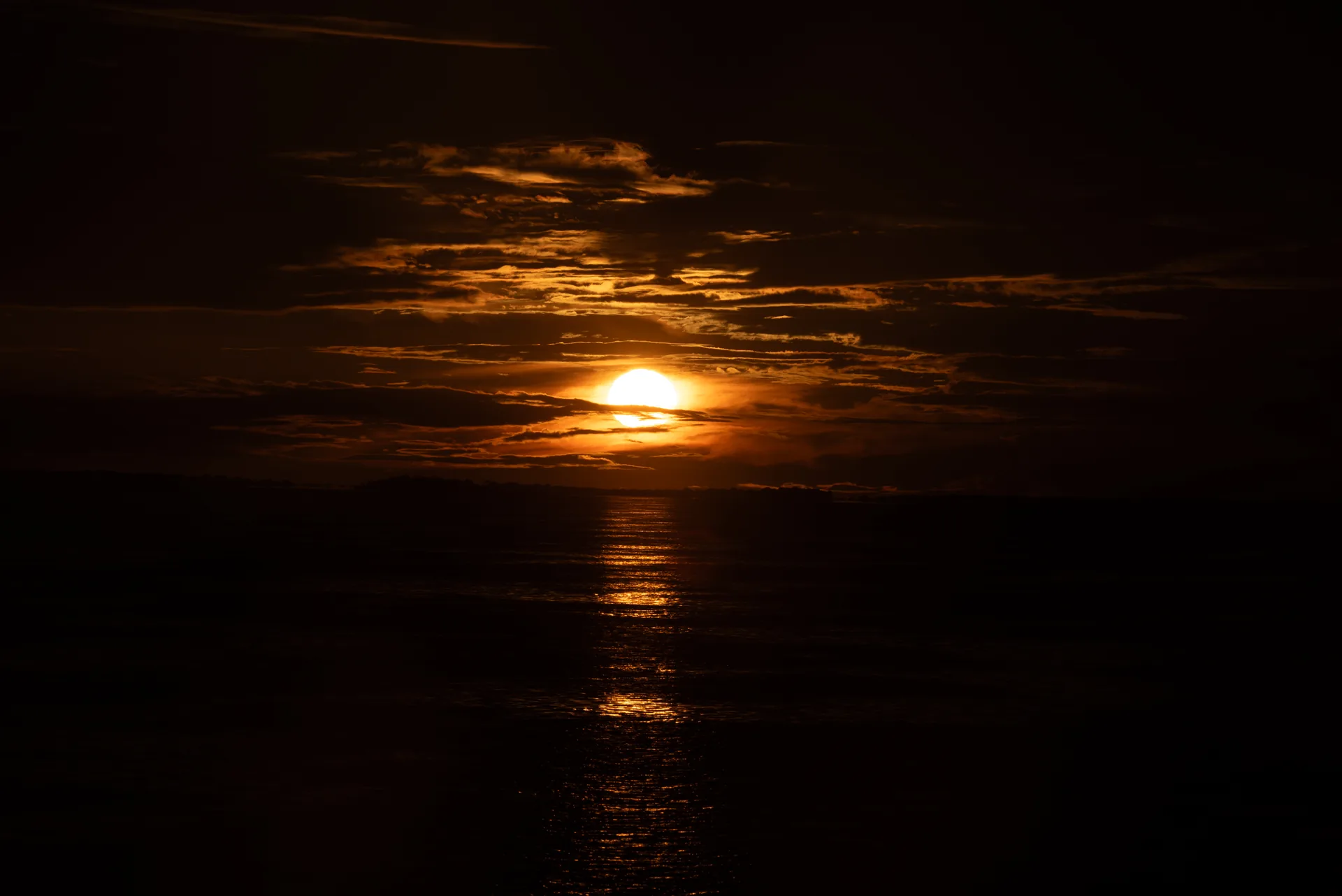 Sol dourado entre nuvens escuras, refletido na água de um rio da Amazônia