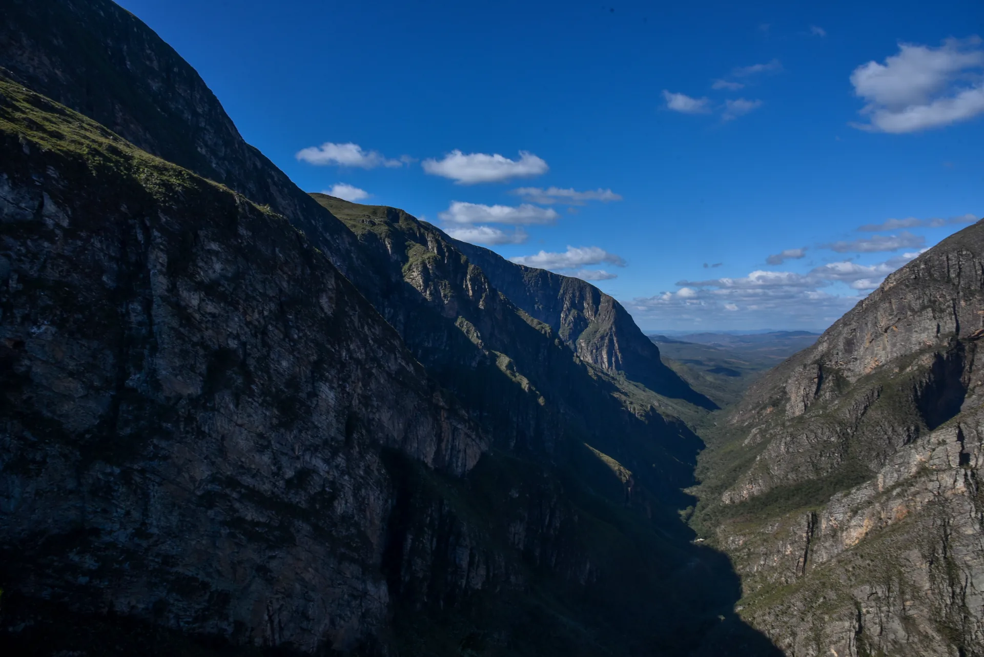 Cânion de paredões escuros se abrindo para o horizonte sob céu azul, no Vale do Travessão